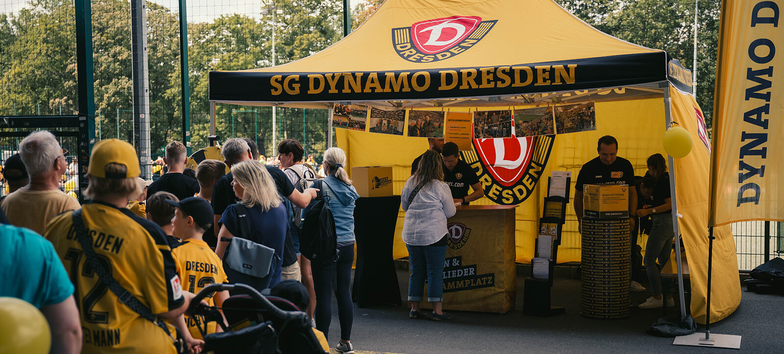 Eine Menschenmenge steht vor einem aufgebauten Stand, der Stand hat die Farben und die Aufschrift des Clubs SG Dynamo Dresden.